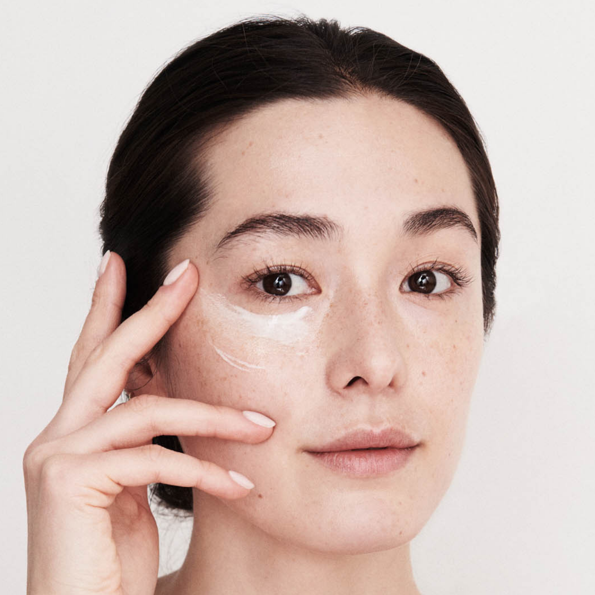 Woman applying cream to her face with a neutral background