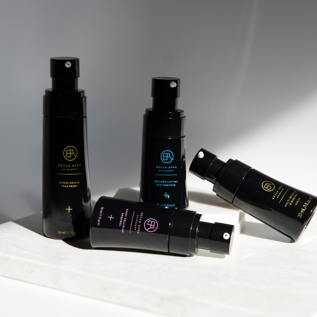 Four sleek Bella Aura skincare spray bottles arranged in natural light, highlighting the elegant black packaging.