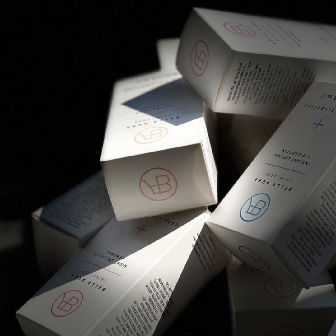 Stacked Bella Aura product boxes in minimalist packaging with embossed logos and a sleek, luxurious design.