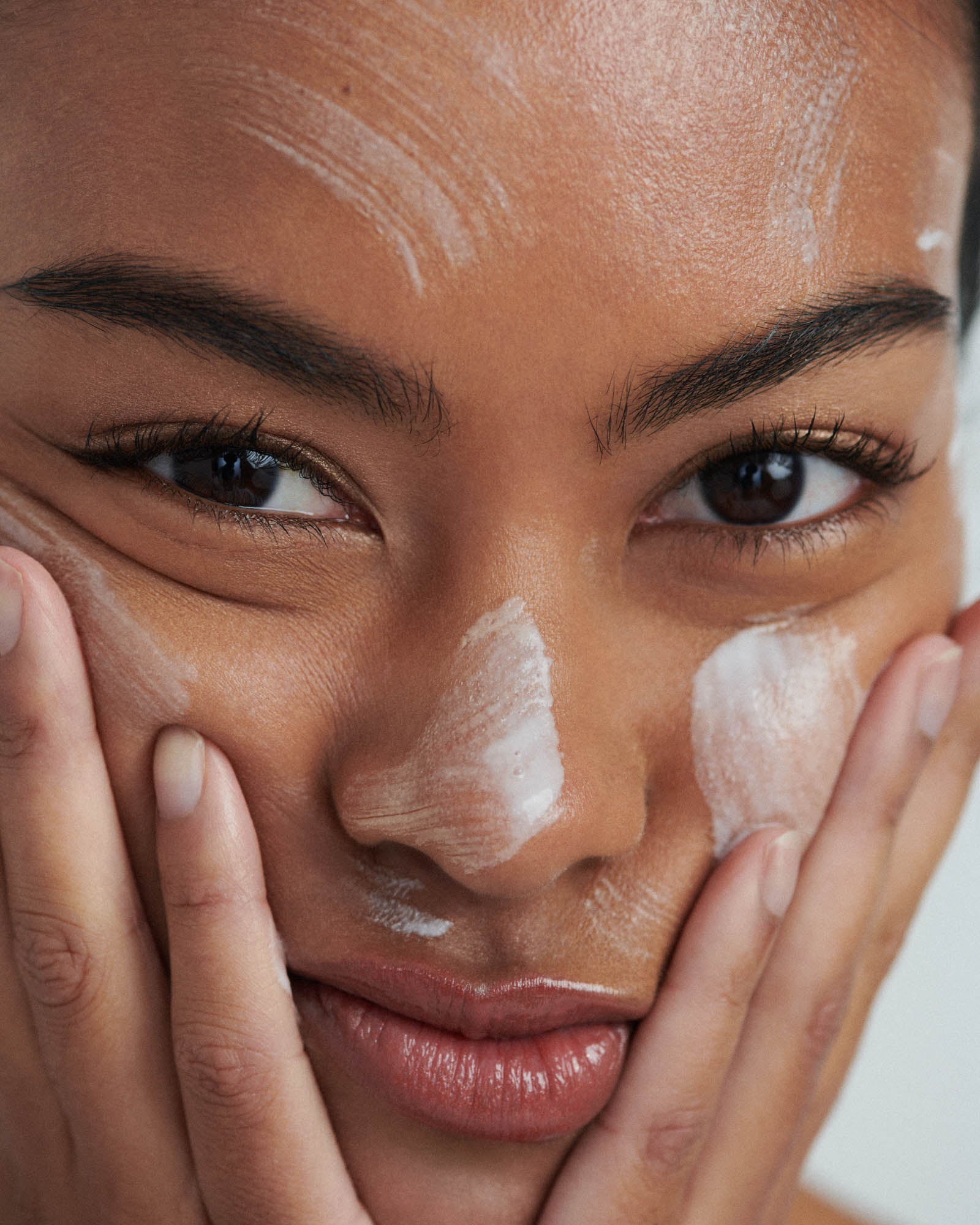 Model applying skincare product to her face, illustrating Bella Aura's Prevent product designed to enhance skin clarity and texture