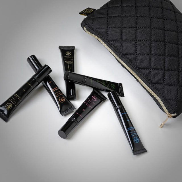 A selection of Bella Aura skincare tubes spilled from a black quilted pouch, emphasizing the travel-friendly design.